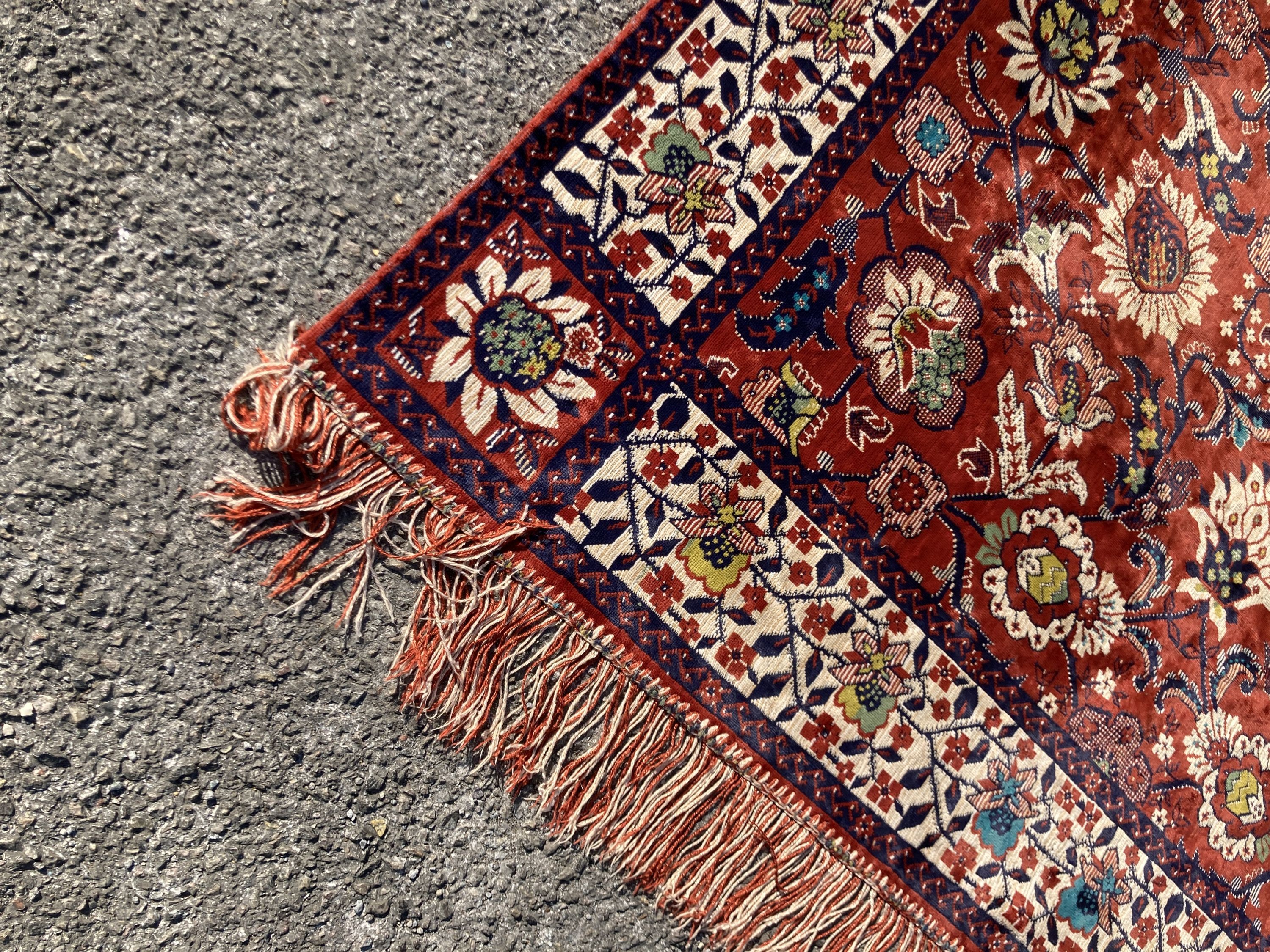 A large embroidered silk rug with a claret red ground interspersed with symmetrical foliate decoration, 136 x 260cm